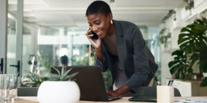 A businesswoman talking on the phone, smiling, and looking at a laptop.