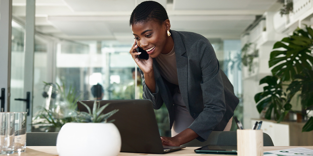A businesswoman talking on the phone, smiling, and looking at a laptop.